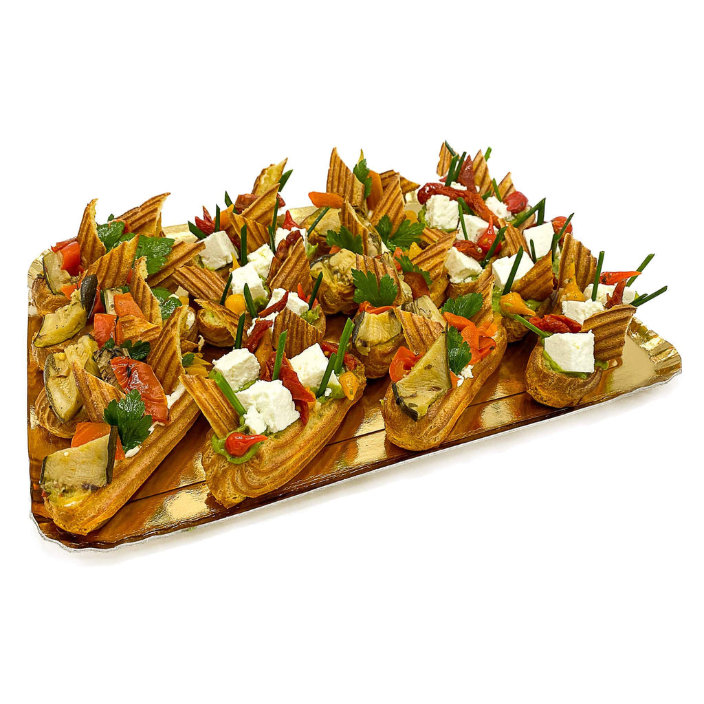 Kleine Eclair mit Avocado, Tomaten, Antipasti und Fetakäse auf goldener Platte.