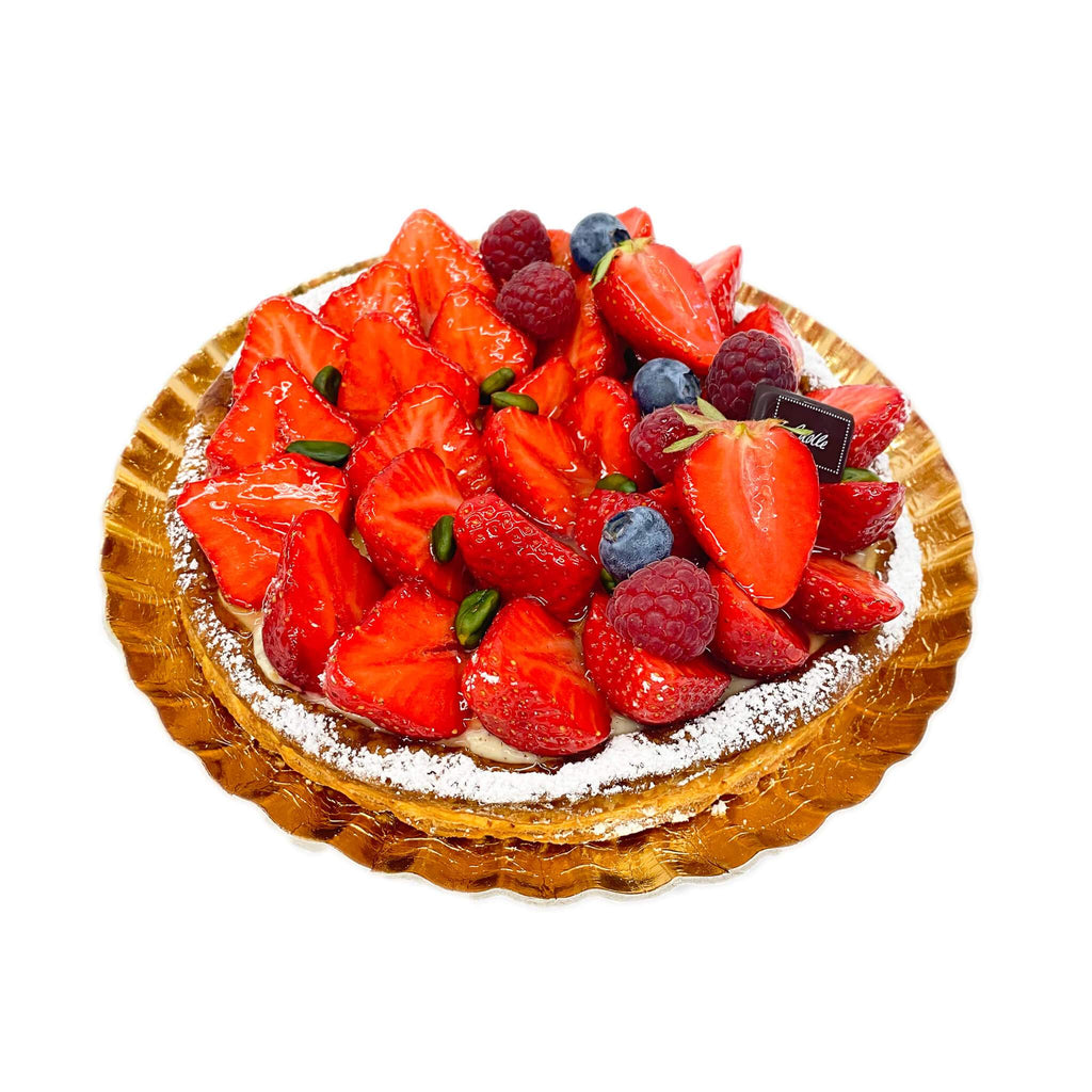 Tarte aus Butterblätterteig, gefüllt mit Vanillecreme, belegt mit Erdbeeren und dekoriert mit Himbeeren, Heidelbeeren und Pistazien auf Goldteller
