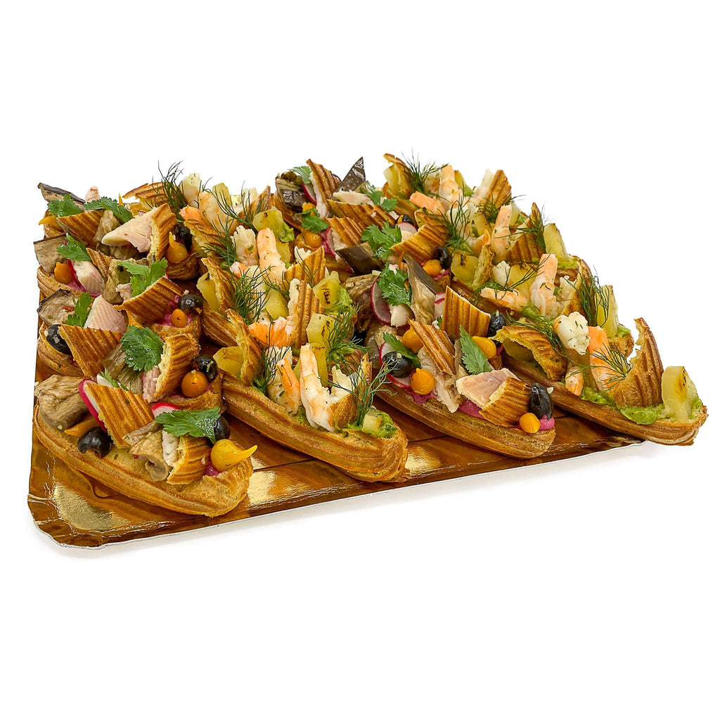 Kleine Eclair mit Garnelen, Avocado, Forelle, Aubergine und Ananas auf goldener Platte.